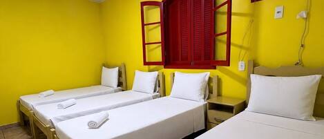 A hotel room with three single beds, a red-framed window, and a wall-mounted air conditioning unit.