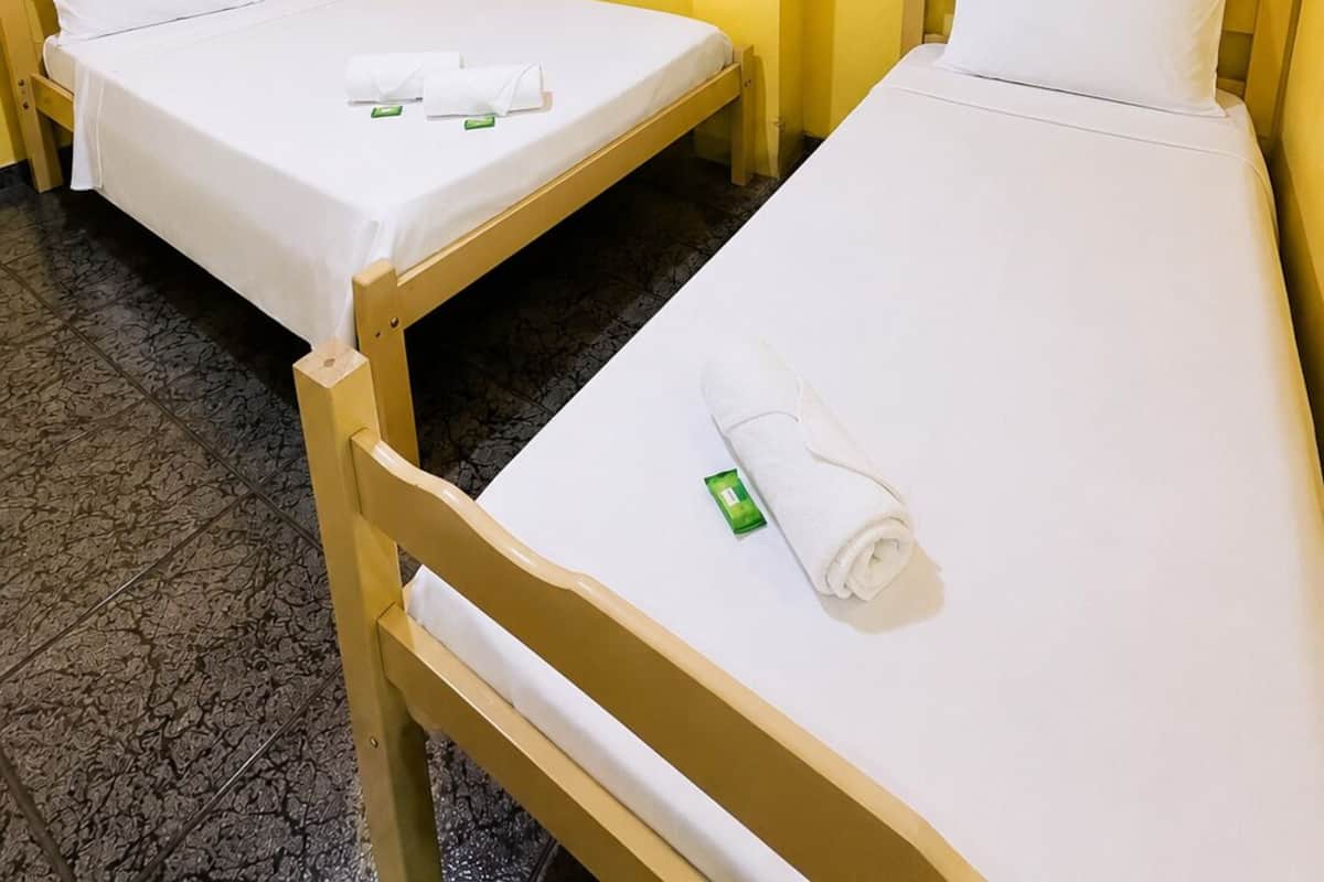 Zwei Einzelbetten mit weißen Laken, ein Fenster mit rotem Rahmen und eine Wand-Klimaanlage.