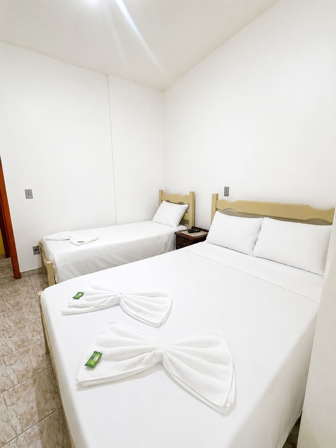 A hotel room with two single beds, a wooden headboard, a nightstand, and a bathroom door.