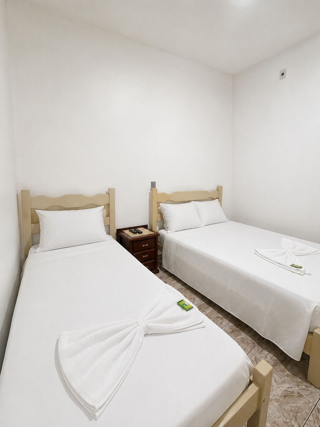 A hotel room with two single beds, a small wooden nightstand, and a neatly made bed with a towel.