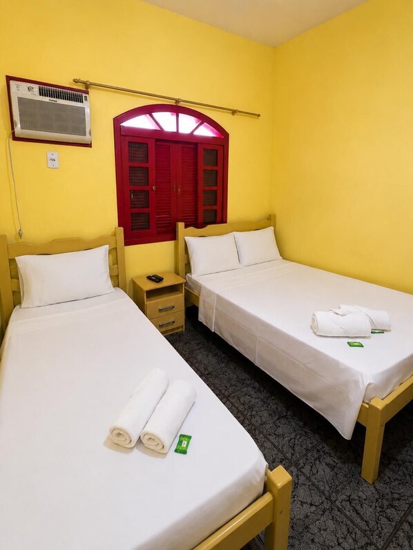 A room with two beds, a red door, an air conditioning unit, and a small bedside table with a lamp.