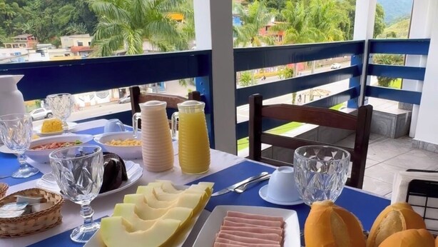 Una mesa de desayuno con comida y bebidas, vistas a zonas verdes y edificios, y una barandilla de balcón.