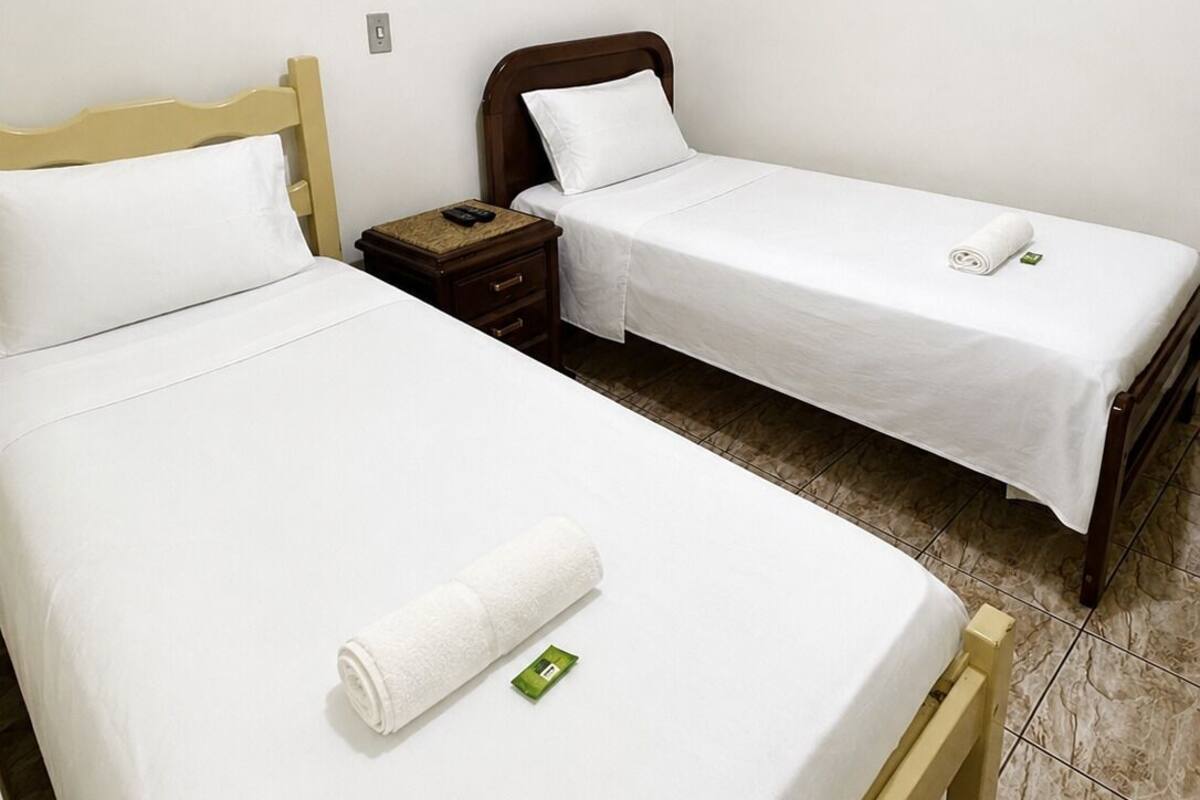 Ein Zimmer mit zwei Einzelbetten, einem Holznachttisch mit Telefon und einem kleinen Tisch mit Handtuch.