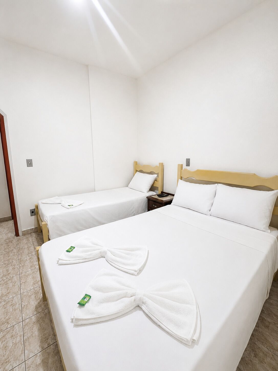 Habitación de hotel con dos camas individuales, cabecero de madera, mesita de noche y puerta de baño.