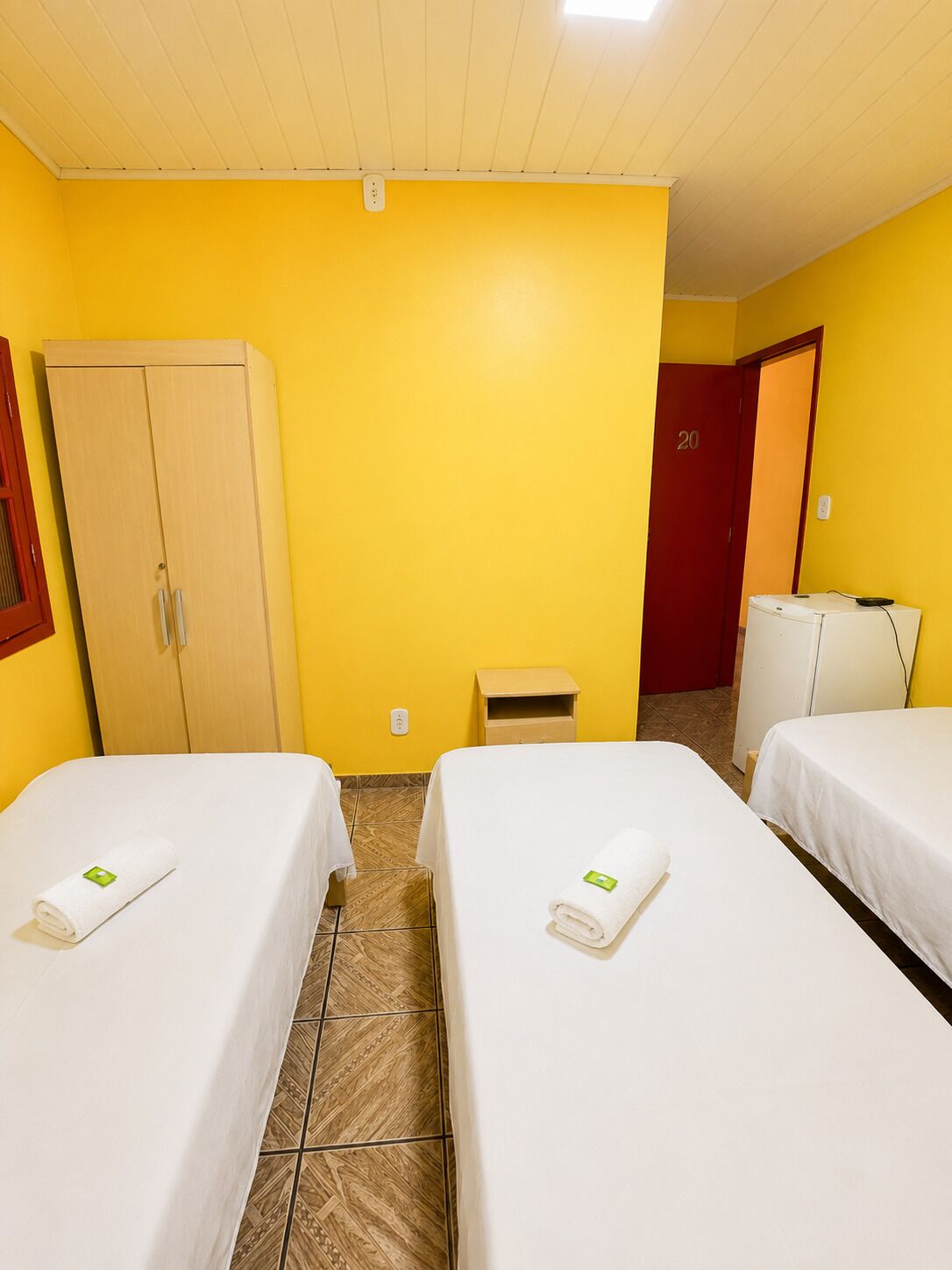 A hotel room with two beds, a wardrobe, a small table, and a red door.