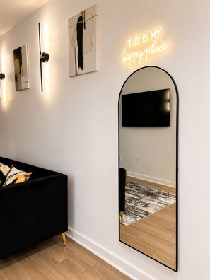 A modern living room with a black sofa, a large mirror, and a neon sign. - Luxury Belt Line Retreat l Walk to Ponce City Market & Krog Street (Atlanta)