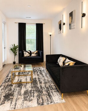 Een moderne woonkamer met een zwarte bank, een glazen salontafel en een vloerkleed met een patroon.