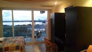 Ein Hotelzimmer mit Bett, Sessel, Fernseher und großem Fenster mit Blick auf ein Gewässer und Stadtlandschaft.