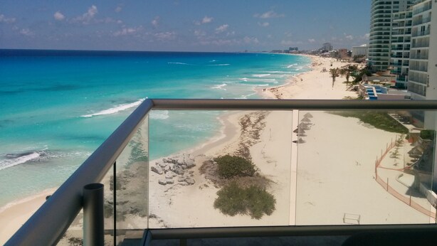 Blick auf einen Strand vom Balkon aus, mit klarem türkisblauem Wasser, Sandstrand und Hochhäusern im Hintergrund.