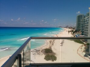 Blick auf einen Strand vom Balkon aus, mit klarem türkisblauem Wasser, Sandstrand und Hochhäusern im Hintergrund.