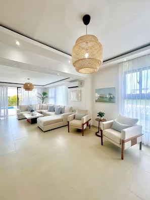 A modern living room with a sectional sofa, armchairs, a coffee table, and a large window with curtains. - Luxury Villa in Punta Cana - Casa Monika (Punta Cana)