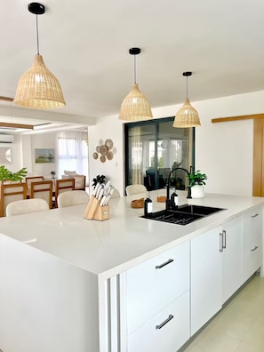 A modern kitchen with white cabinetry, a central island, and three wicker pendant lights. - Luxury Villa in Punta Cana - Casa Monika (Punta Cana)