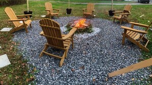 A fire pit surrounded by Adirondack chairs in a gravel area with a house in the background. - Fire Pit Evenings • Outdoor Dining - Five Acres (Palenville)