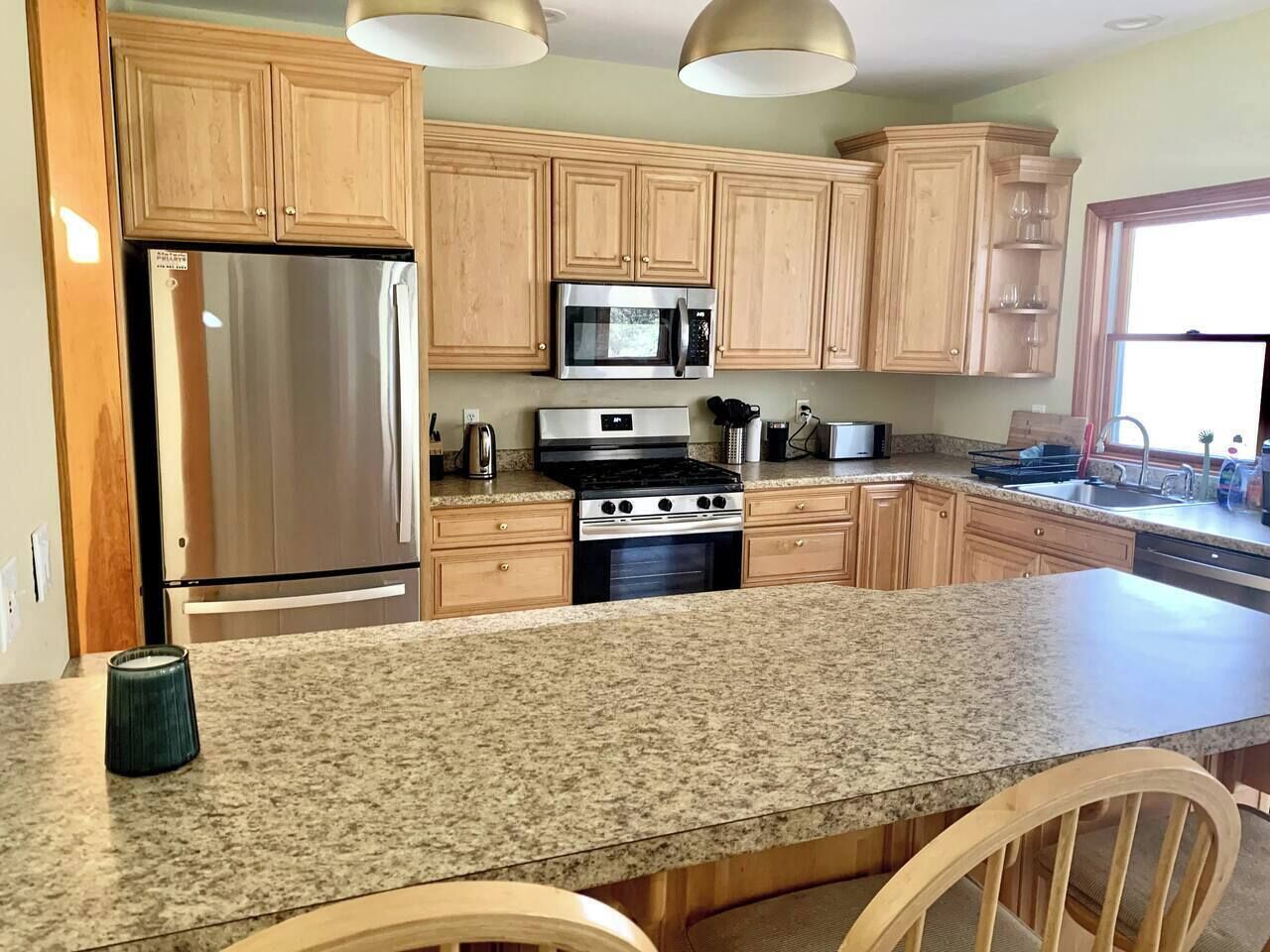 A kitchen with wooden cabinets, stainless steel appliances, granite countertops, and pendant lighting.