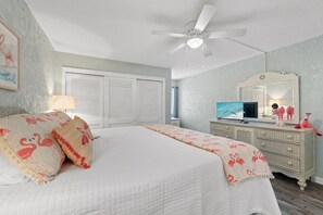 Une chambre à coucher comprenant un lit, un ventilateur de plafond, une commode, un miroir et un téléviseur.