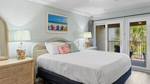 Ein Schlafzimmer mit Bett, Nachttisch, Lampe, einem Gemälde und einem Balkon mit Sitzmöbeln.