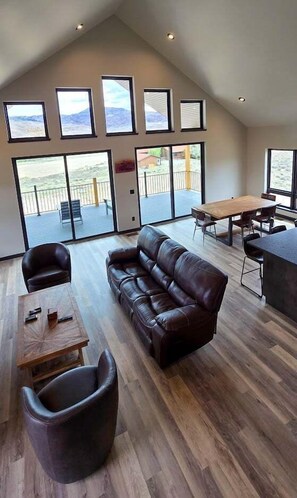 Ein großzügiger Wohnbereich mit Ledersofa, Couchtisch und Esstisch mit Stühlen. Große Fenster bieten Ausblick ins Freie.
