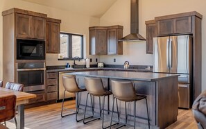 Een moderne keuken met houten kastjes, roestvrijstalen apparatuur, een groot eiland met barkrukken en een raam voor natuurlijk licht.