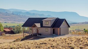 A modern two-story house with a sloped roof, a covered porch, and a view of the surrounding landscape. - LaLuna Ranch- 4 bedroom mountain-view home on the way to Yellowstone (Cody)