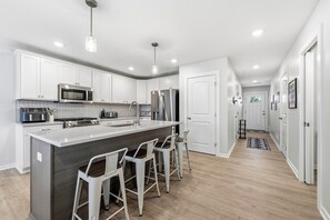 A modern kitchen with white cabinets, stainless steel appliances, and a bar area with stools. - Game Night- Game themed vacation rental (South Haven)