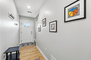 A hallway with a white door, a staircase, and framed artwork on the walls. - Game Night- Game themed vacation rental (South Haven)