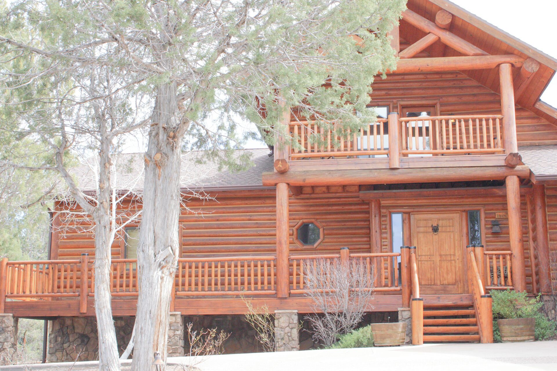 A log cabin with a balcony, a front door, and a stone foundation.