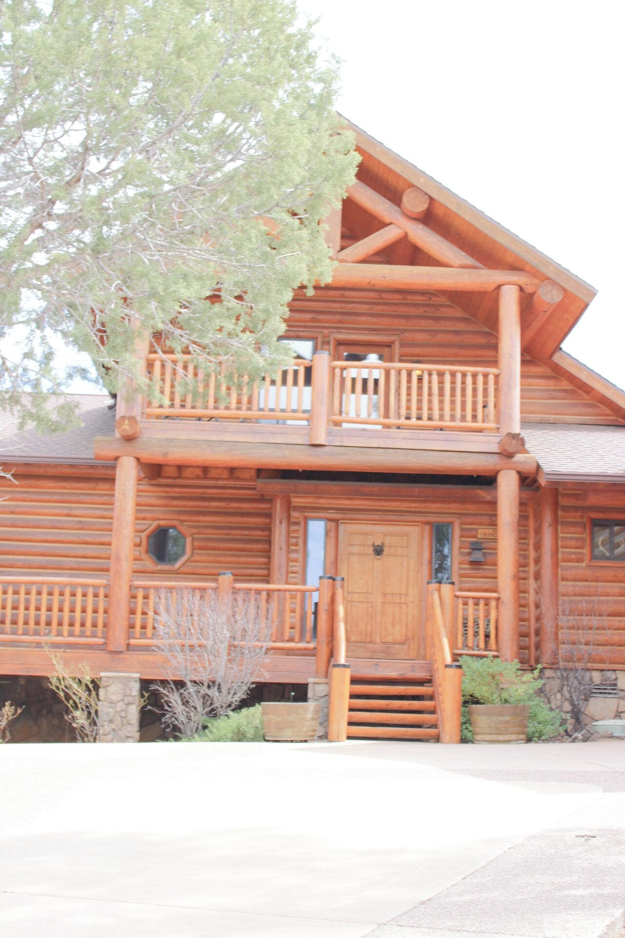 A two-story log cabin with a balcony, a front door, and a stone foundation.