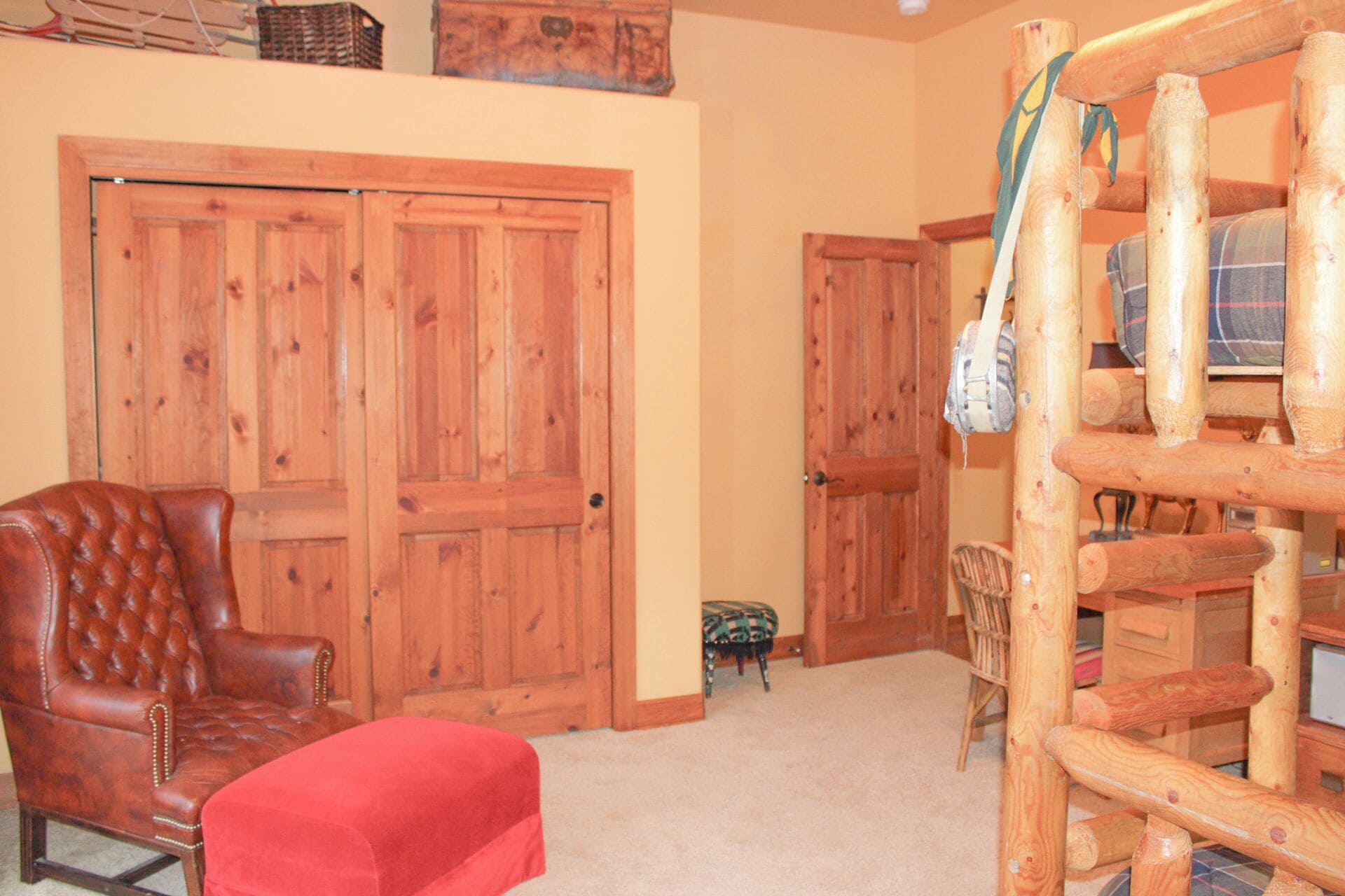 Quarto com porta de madeira grande, poltrona de couro, banquinho vermelho, um apoio para os pés pequeno e uma estrutura de madeira para brincar.