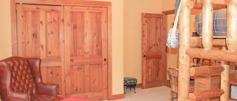 Quarto com porta de madeira grande, poltrona de couro, banquinho vermelho, um apoio para os pés pequeno e uma estrutura de madeira para brincar.