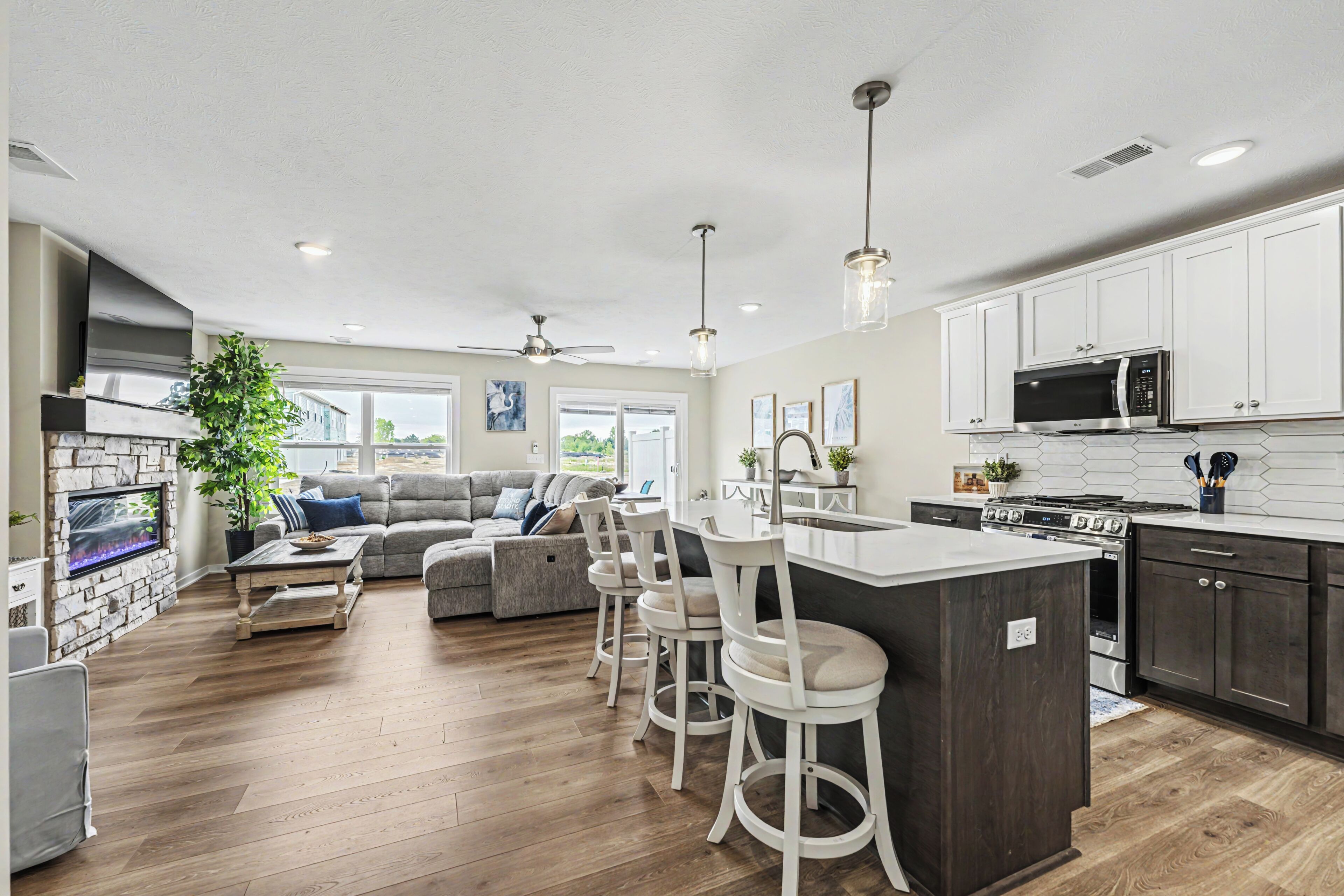 Une cuisine moderne avec des meubles blancs, un îlot central doté de tabourets, un four à micro-ondes encastré et une cuisinière.