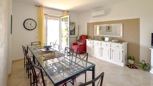 Un comedor con una mesa de vidrio, sillas, una silla roja, un armario blanco y un reloj en la pared.