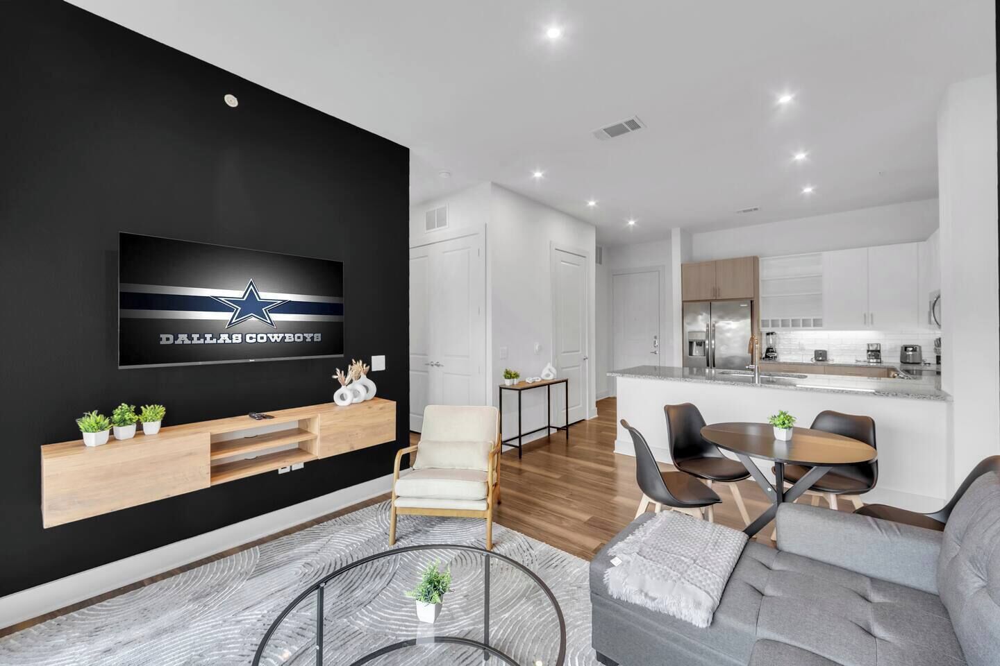 Een moderne woonkamer met een flatscreen televisie, een bank, een salontafel en een eethoek met een tafel en stoelen.