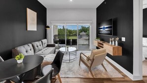 A modern living room with a grey sofa, a dining table, and a TV mounted on the wall. - ToyotaStadium+Pool+Gym+PGAGolf+FriscoSquare+W+D (Frisco)