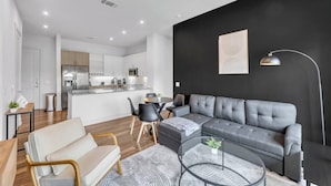 A modern living space with a grey sofa, a dining table, and a kitchen area. - ToyotaStadium+Pool+Gym+PGAGolf+FriscoSquare+W+D (Frisco)