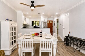 A dining area with a white table set for four, surrounded by white chairs, a ceiling fan, and a view of the kitchen in the background. - 2BR Silverado CC condo with golf views, pool, patio, and fireplace. (Napa)