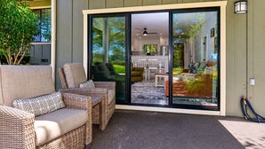 Un patio cubierto con mobiliario de mimbre, una puerta corrediza de vidrio que da a un espacio interior y una manguera en el suelo.