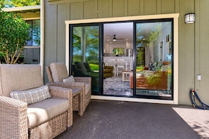 A covered patio area with wicker furniture, a sliding glass door leading to an indoor space, and a hose on the ground.