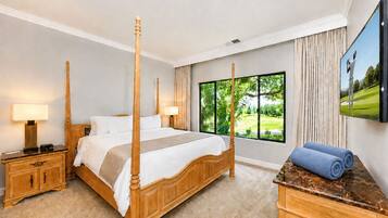 A four-poster bed with a wooden headboard, a nightstand with a lamp, a wooden dresser, and a large window with a view of greenery.