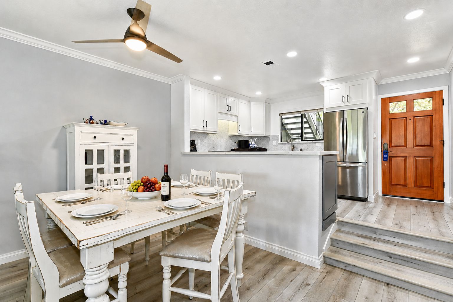 A kitchen with white cabinetry, a dining table set for six, and a stainless steel refrigerator.