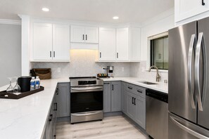 A modern kitchen with white cabinetry, stainless steel appliances, and a marble countertop.