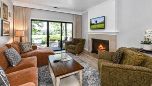Una sala de estar con chimenea, televisor montado arriba y un amplio ventanal con vistas al exterior.