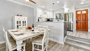 Una cocina con armarios blancos, una mesa de comedor para cuatro, un refrigerador y una puerta de madera.