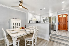 A kitchen with white cabinetry, a dining table set for four, a refrigerator, and a wooden door.