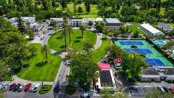 An aerial view of a golf course with a tennis court, parking area, and a building with a red roof.