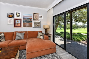 A modern living room with a sectional sofa, a coffee table, and a large window offering a view of a golf course.
