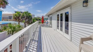 Puinen terassi, jossa on valkoiset kaiteet, punainen aurinkovarjo ja ulkokalusteita.