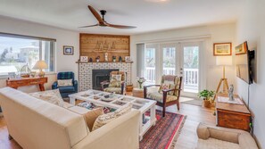 A living room with a fireplace, a ceiling fan, and a large window. - Turtlemound Terrace - Your Favorite Beach Getaway (New Smyrna Beach)