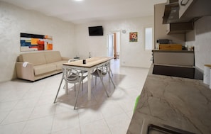 Un salon moderne comprenant un canapé, une table à manger et des chaises, une cuisine avec une cuisinière et des placards, et un téléviseur fixé au mur.