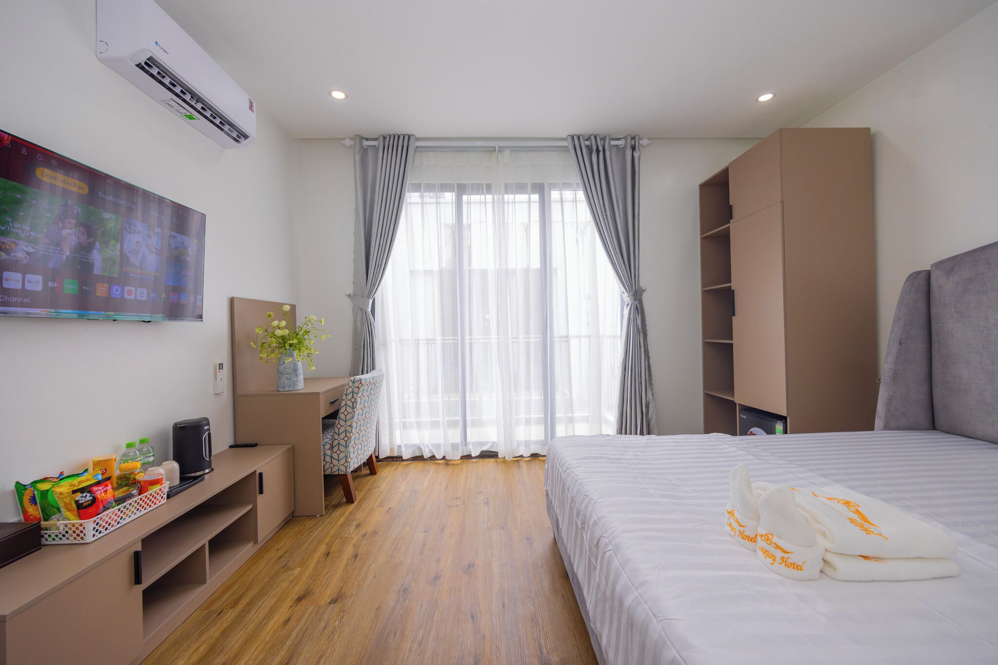 Ein Hotelzimmer mit Bett, Fernseher, Schreibtisch und einem fensterbelaubten Fenster.