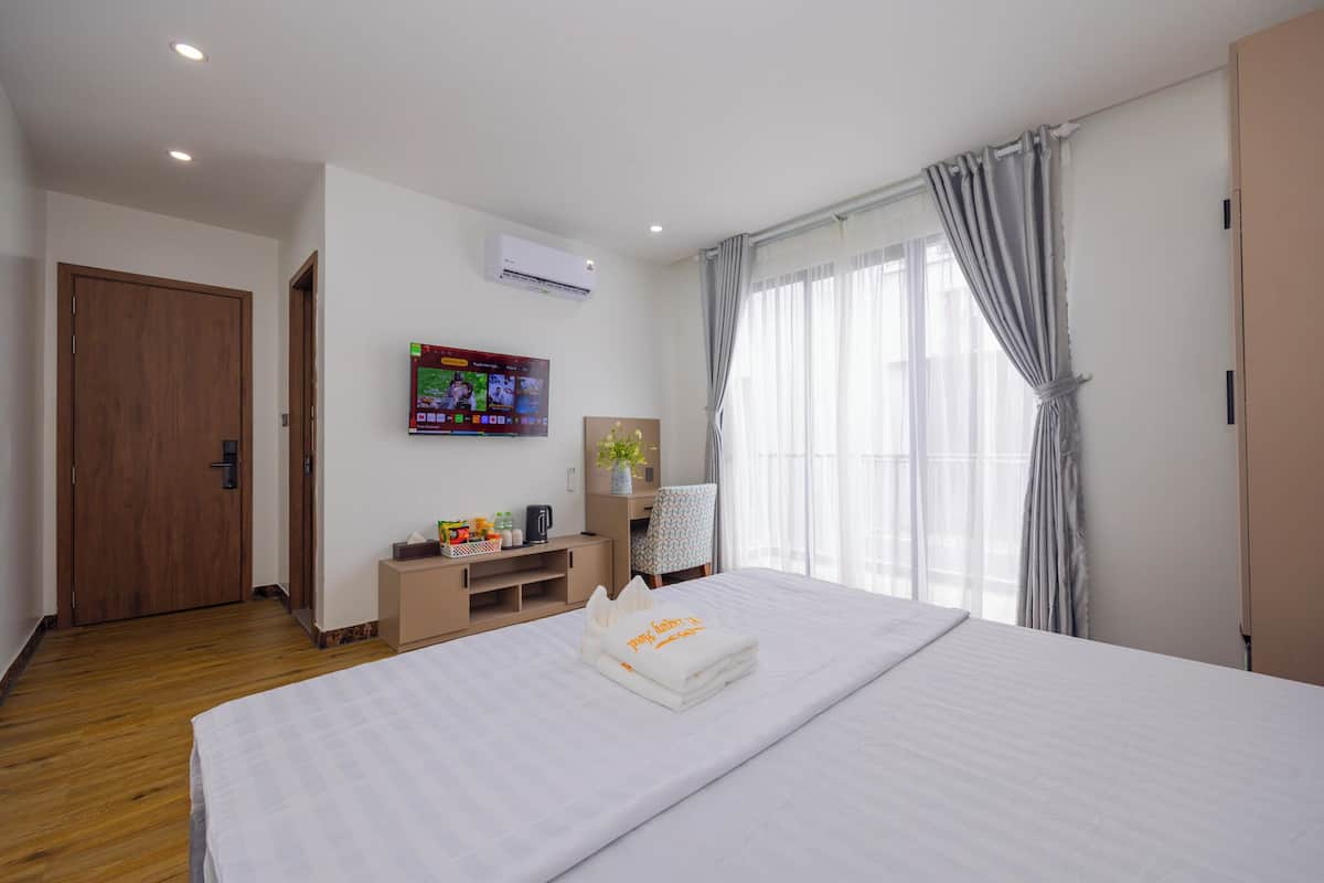 A hotel room with a bed, a TV, a desk, and a window with curtains.